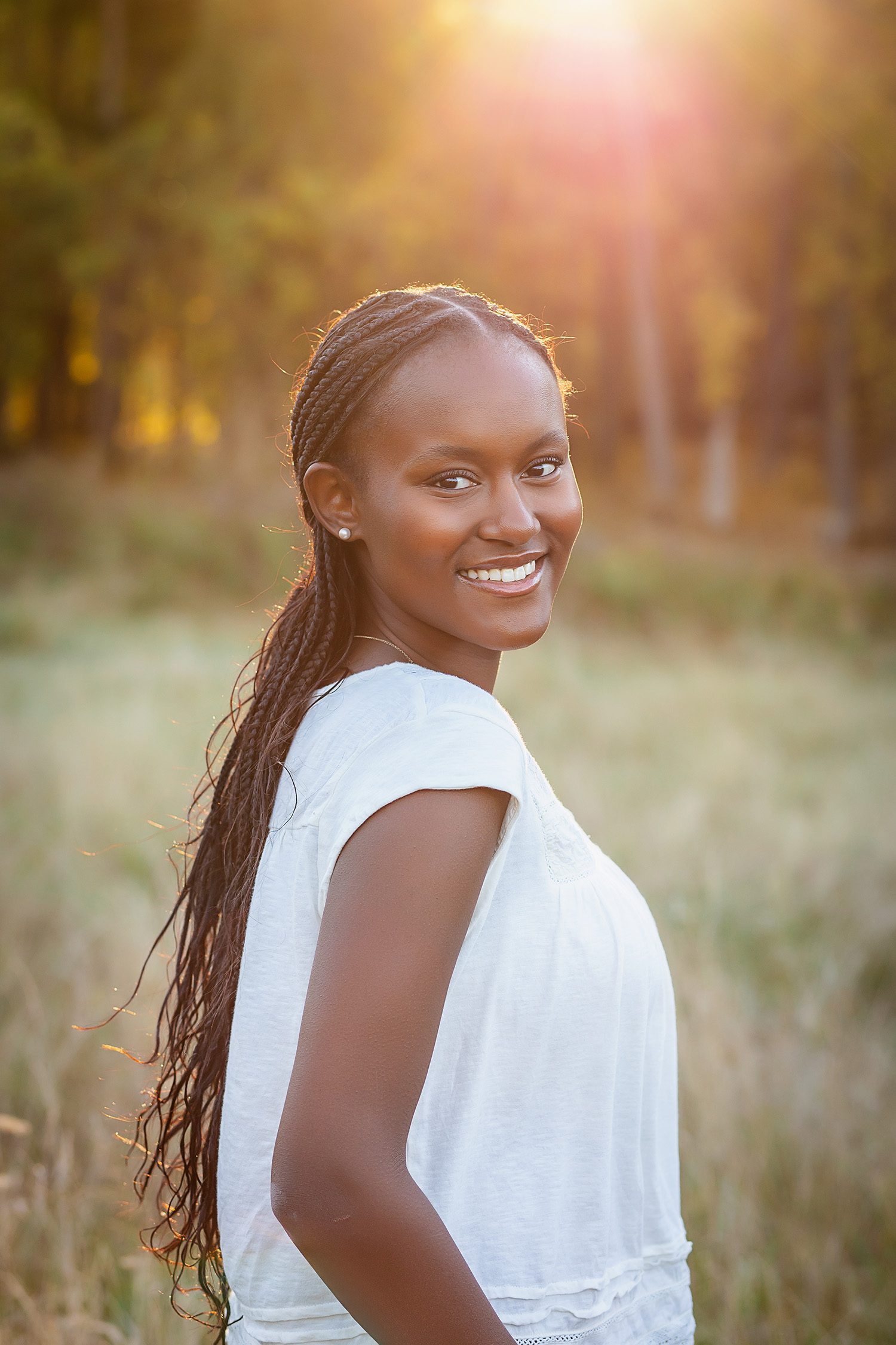 family photographer in rochester ny captures senior portraits for high school senior in a field at sunset