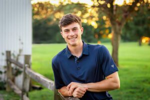 family photographer in rochester ny captures senior portraits for high school senior leaning on a fence at Tinker Park