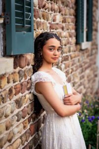 family photographer in rochester ny captures senior portraits for high school senior against a cobblestone house at Tinker Park