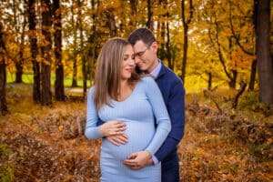 maternity photographer in rochester ny captures expectant parents holding mom's baby bump in a fall sunset