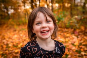 family photographer in rochester ny captures little girl laughing in the fall leaves