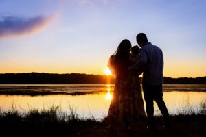 family photographer in rochester ny captures watching the sunset over the water together