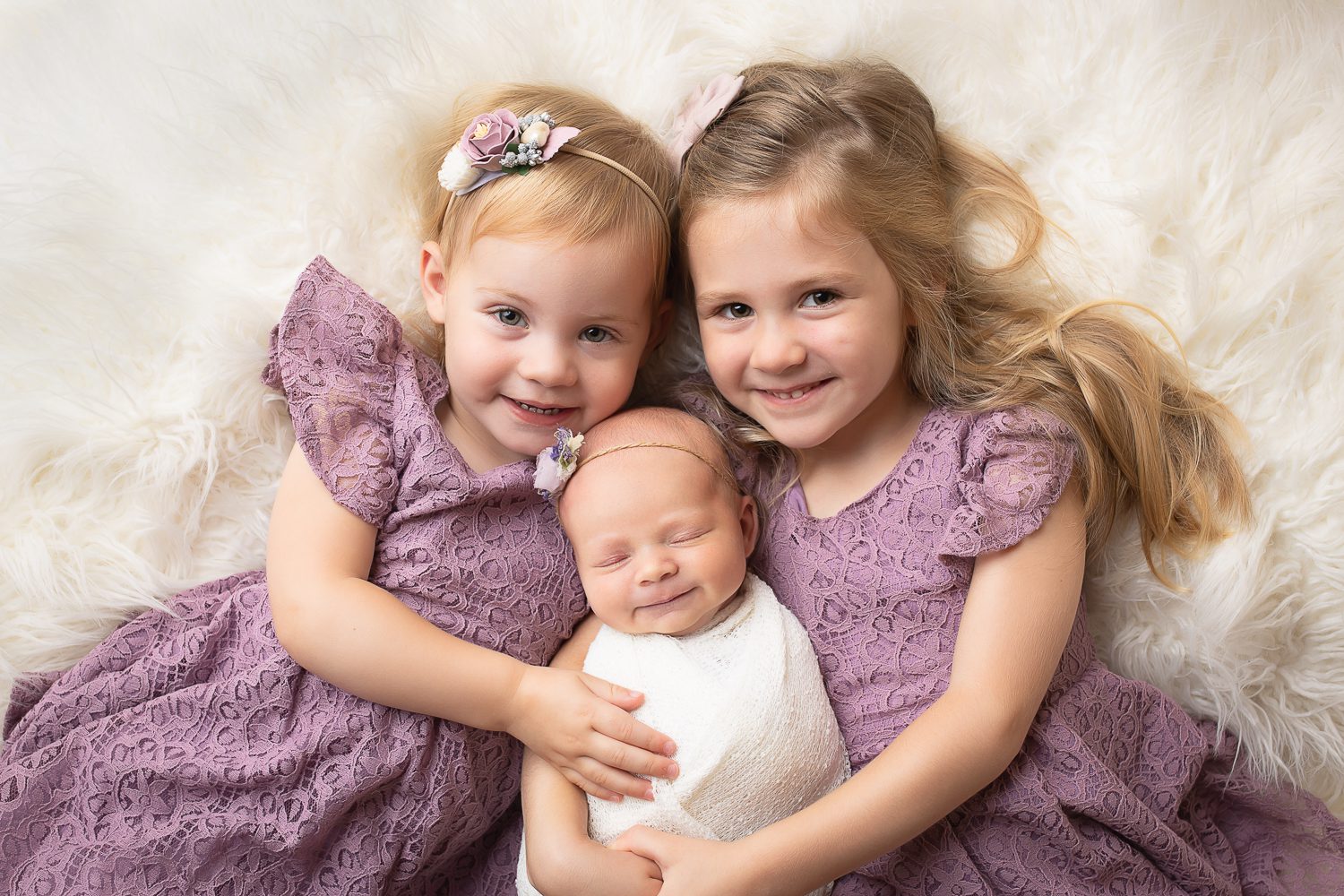 newborn photographer in rochester ny captures newborn baby girl smiling in her big sisters' arms
