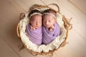 newborn photographer in rochester ny captures twin baby girls sleeping together in a basket