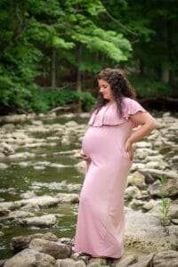 maternity photographer in rochester ny captures pregnant mom holding her baby bump in a creek