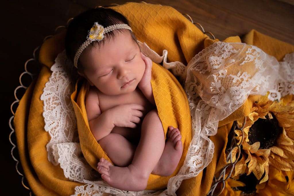 newborn photographer in rochester ny captures newborn baby girl sleeping wrapped in mustard blankets with sunflowers