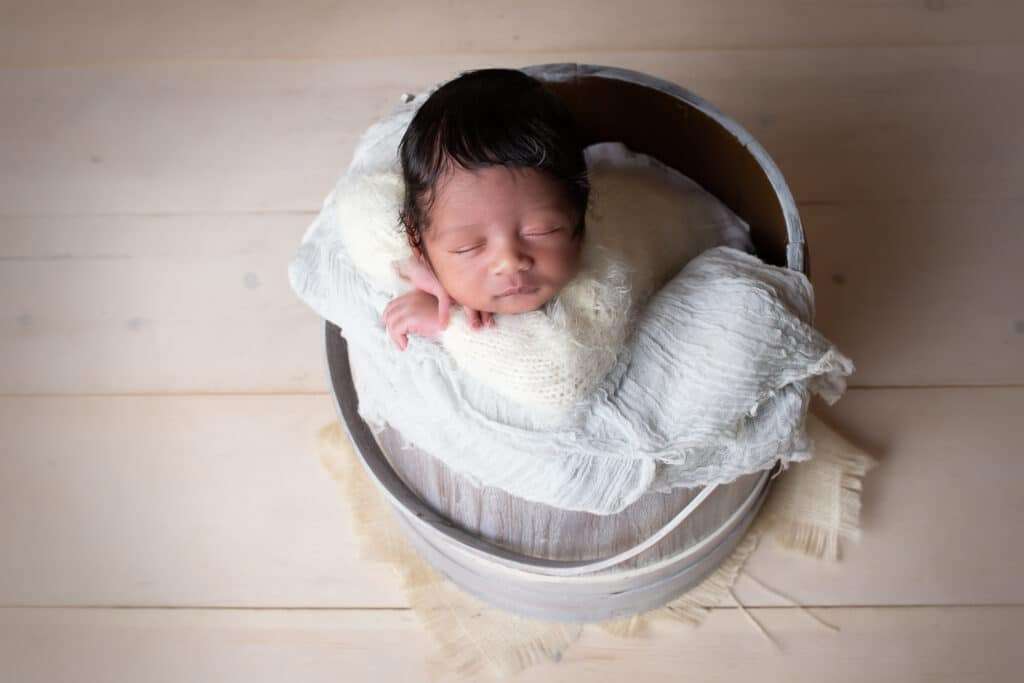 newborn photographer in rochester ny captures newborn baby boy sleeping in a bucket