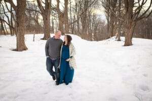maternity photographer in rochester ny captures expectant mom in the snow under the setting sun