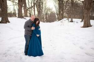 maternity photographer in rochester ny captures expectant mom in the snow under the setting sun