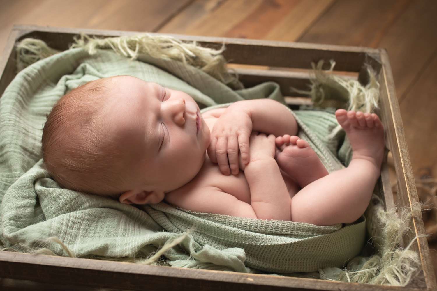 newborn photographer in rochester ny captures newborn baby boy sleeping in a crate
