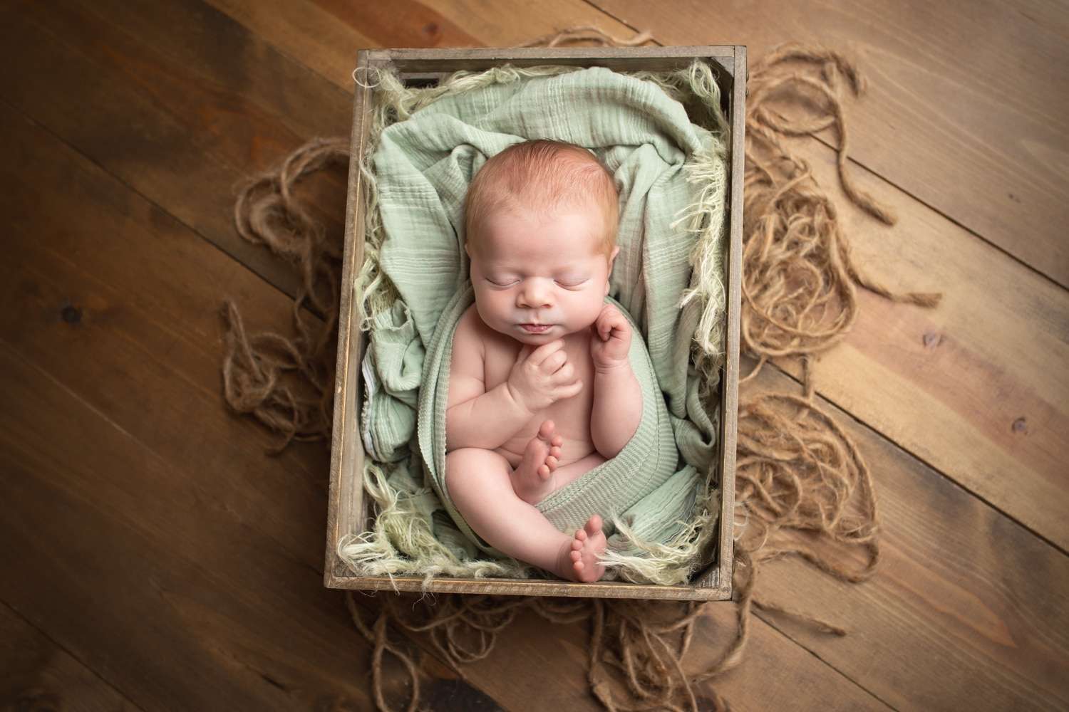 newborn photographer in rochester ny captures newborn baby boy sleeping in a crate
