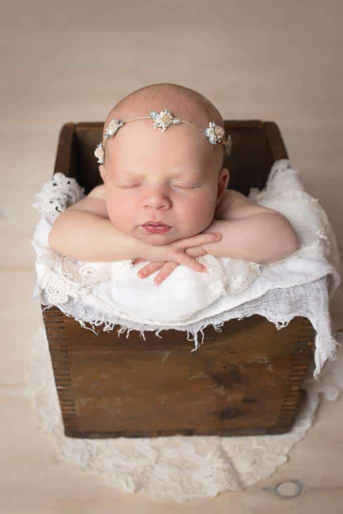newborn photographer in rochester ny captures newborn baby girl with her chin on hands in a crate