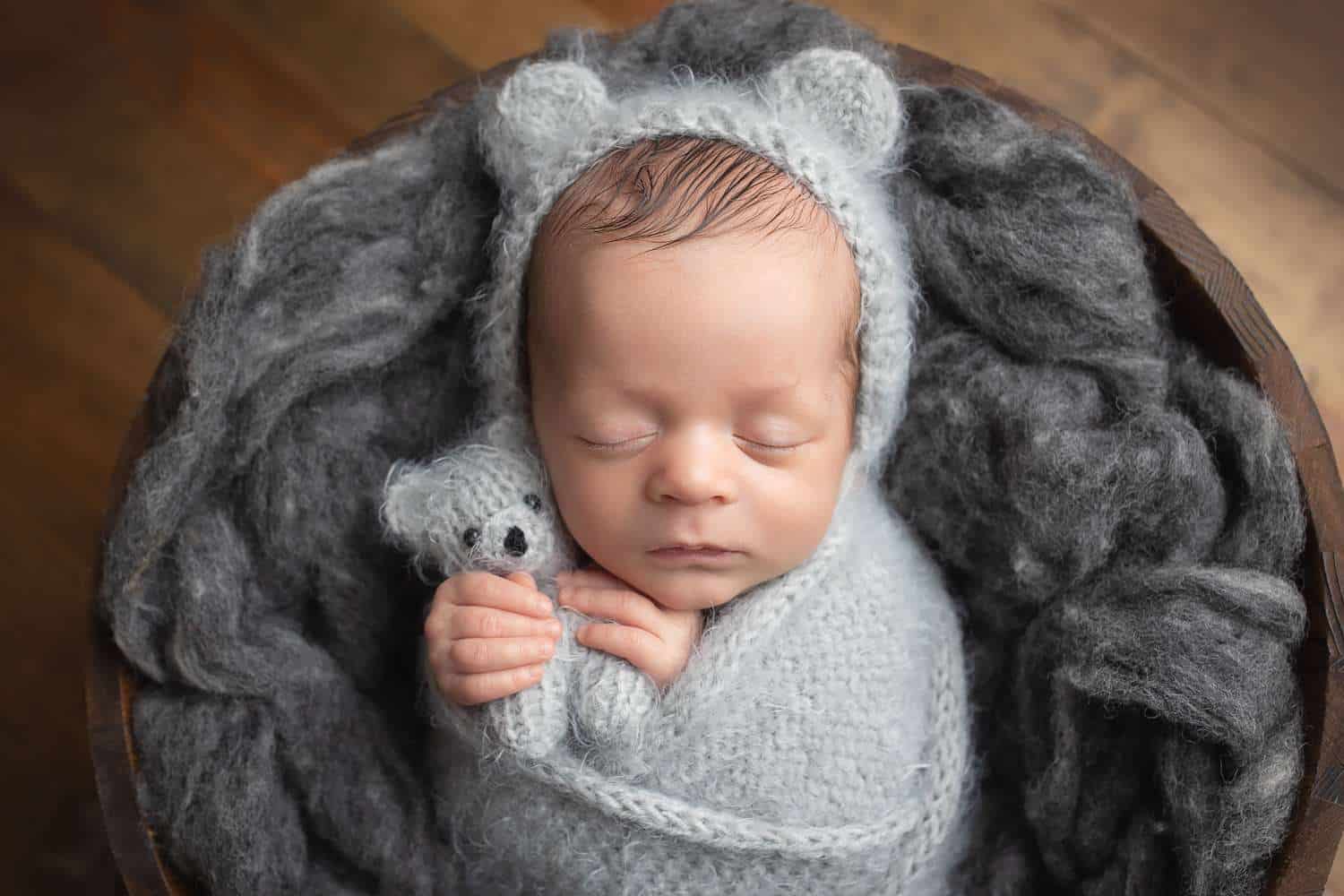 newborn photographer in rochester ny captures newborn baby boy asleep in a bucket wearing a teddy bear bonnet