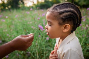 family photographer in rochester ny captures little boy smelling a flower his mom holds for him