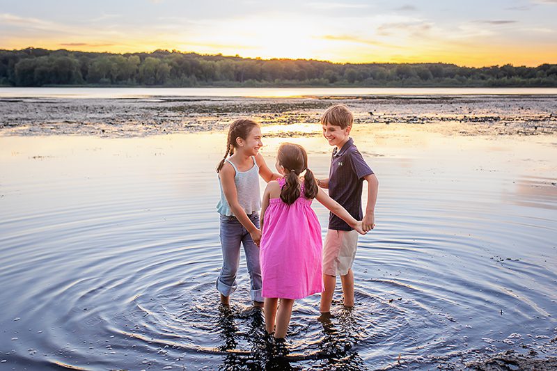 family photographer in rochester ny captures siblings playing together in the pond at sunset