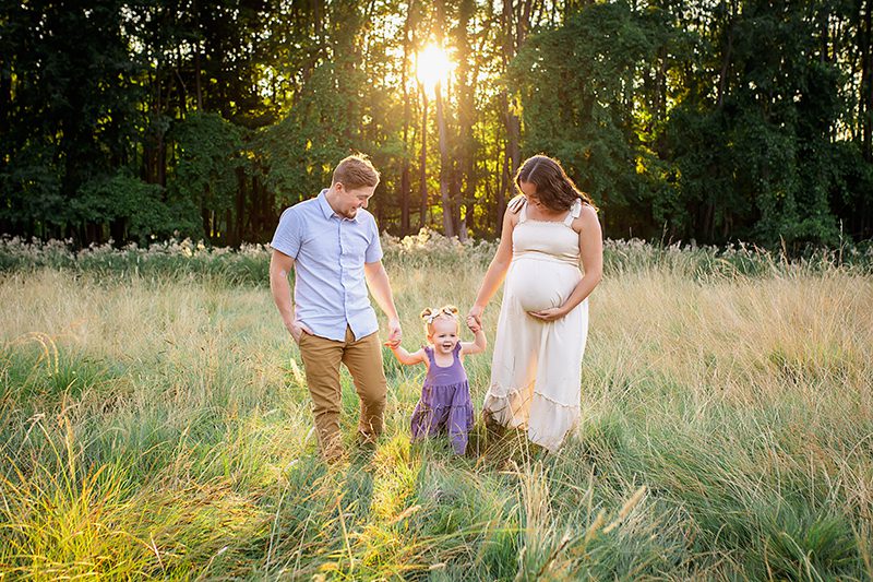 family photographer in rochester ny captures family walking together through a field of tall grasses at sunset